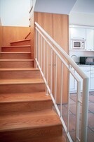 A wooden staircase with white railings leading to a kitchen area with modern appliances.