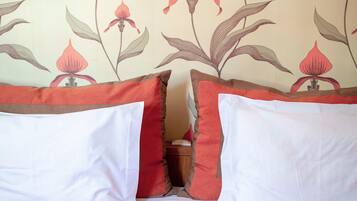 A bed with red bedding and a floral wallpaper pattern.
