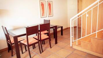 Un comedor con una mesa y sillas de madera, una escalera con barandilla de madera y dos obras de arte enmarcadas en la pared.