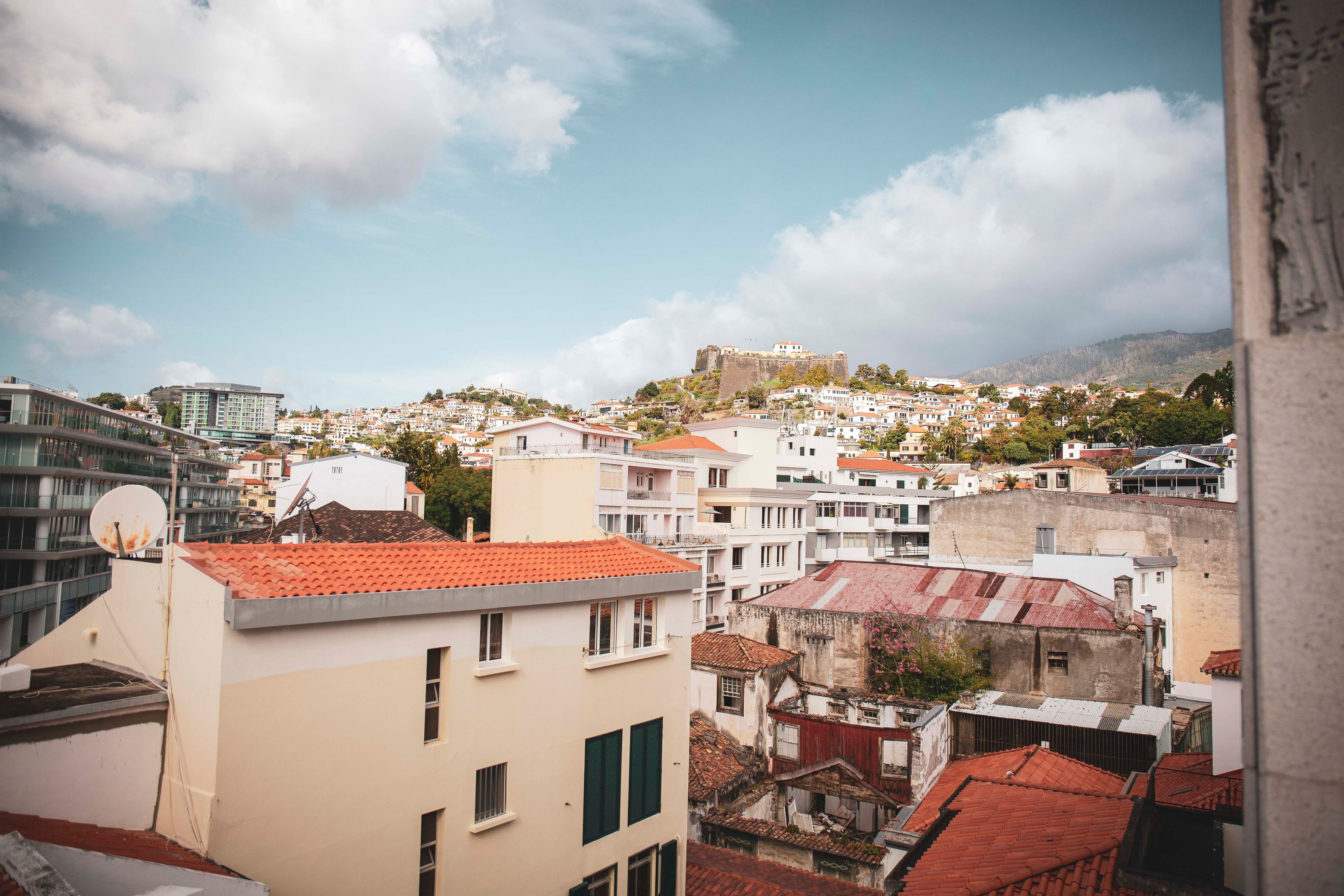 A cityscape with a prominent castle on a hill, surrounded by residential buildings with red-tiled roofs.