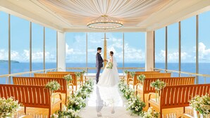 Una ceremonia de boda con vistas al mar, bancos de madera y una araña.