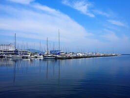 A marina with multiple boats docked, calm water, and a clear sky.