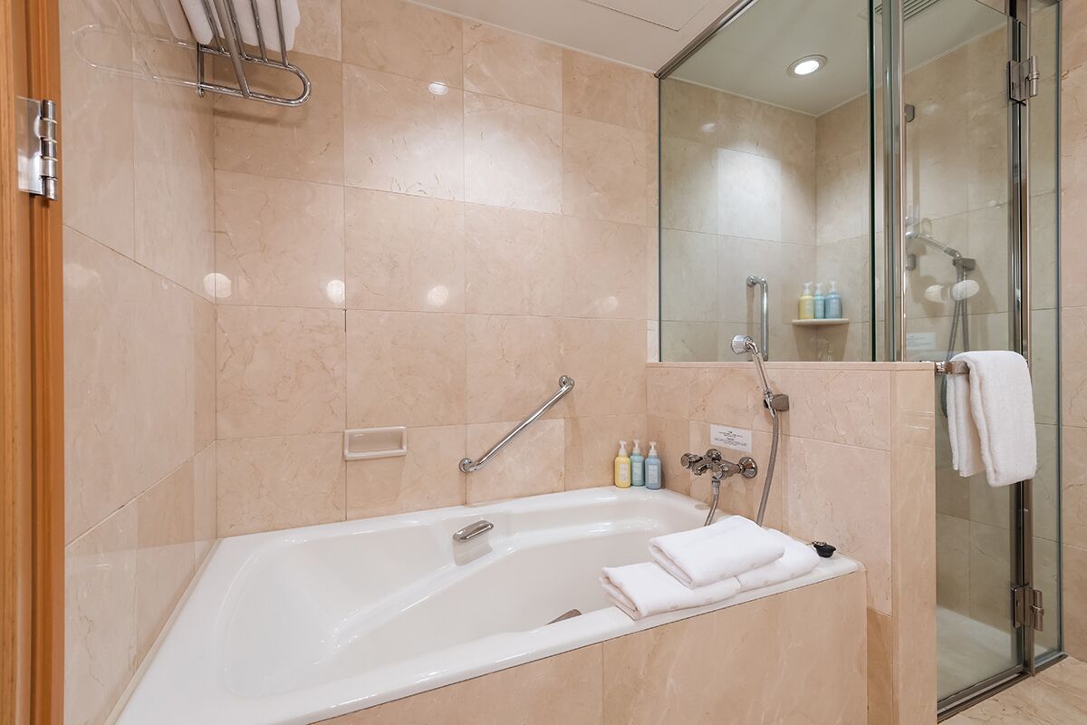 A modern bathroom with a large bathtub, glass shower enclosure, and a shelf with toiletries.