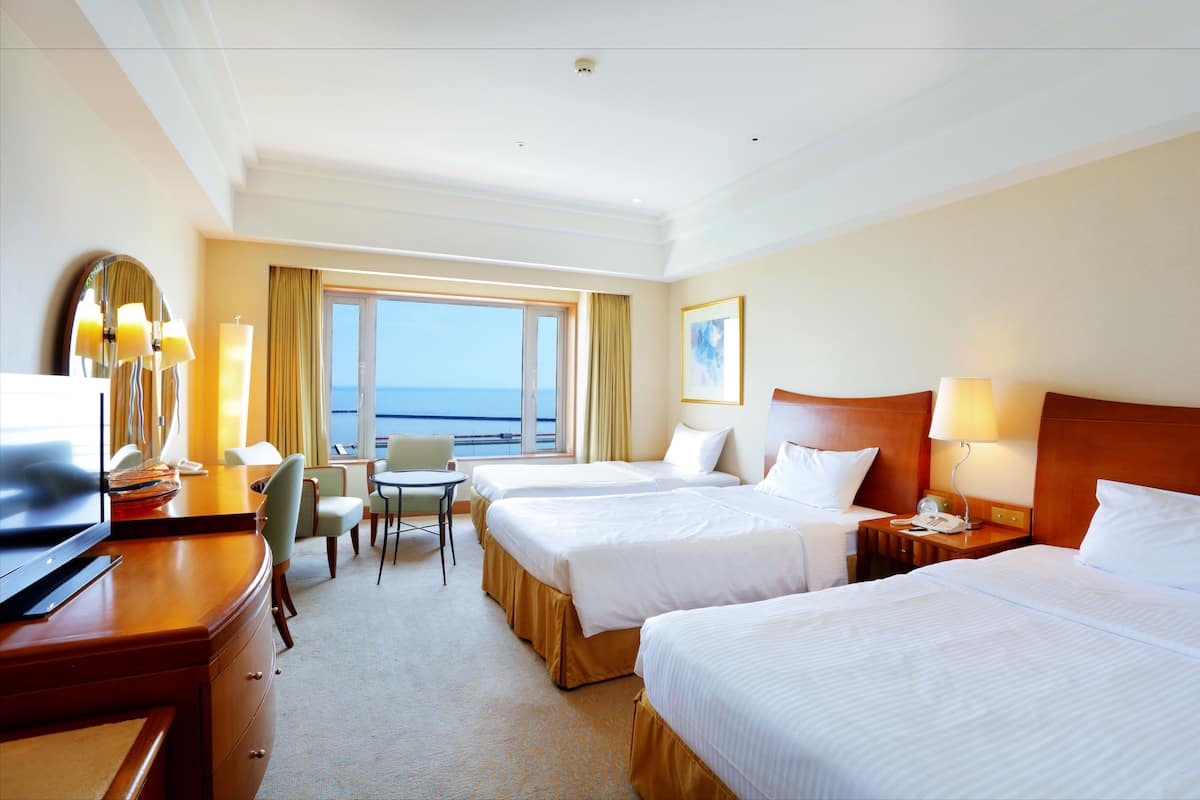 A hotel room with two beds, a desk with a computer, a chair, and a view of the sea.