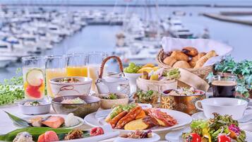 A table set with various dishes, including seafood, bread, and vegetables, with a marina view in the background.