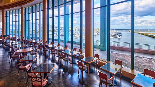 Un amplio comedor interior con grandes ventanales que dan a un puerto deportivo y al paisaje urbano.