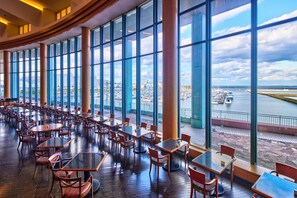 A spacious indoor dining area with large windows overlooking a marina and cityscape.