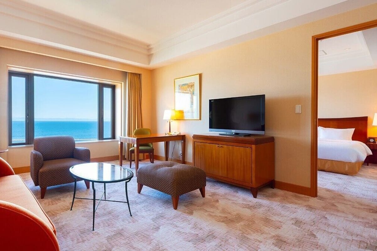 Habitación de hotel con una ventana grande, televisor, sofá, sillón, una mesita y cama.