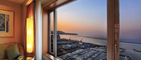 Una habitación con un ventanal grande que da a un puerto deportivo con barcos y vistas al atardecer.