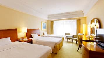 A hotel room with two beds, a desk, a chair, a TV, and a window with curtains.