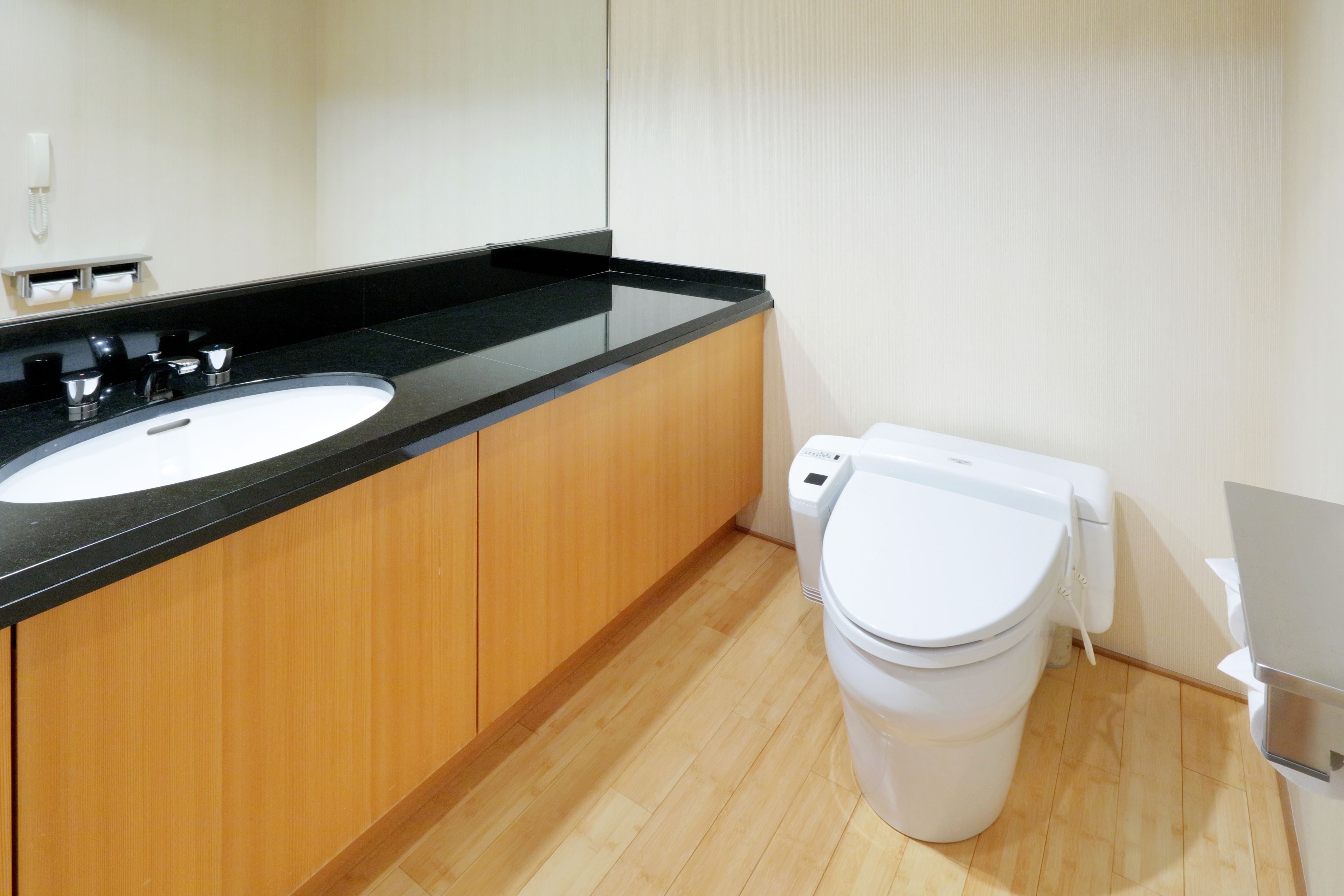 A modern bathroom with a black countertop sink, wooden cabinets, a white toilet, and a mirror.