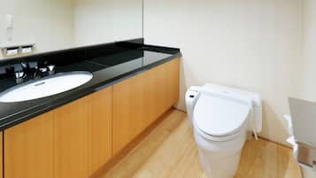 A modern bathroom with a black countertop sink, wooden cabinets, a white toilet, and a mirror.