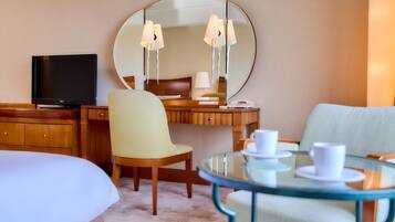 Une chambre d’hôtel avec un lit, un bureau avec un ordinateur, une chaise, une petite table ronde en verre avec des tasses, et un grand miroir au mur.