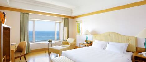 Habitación de hotel con una cama grande, un escritorio, una silla, una mesita y vistas al mar.