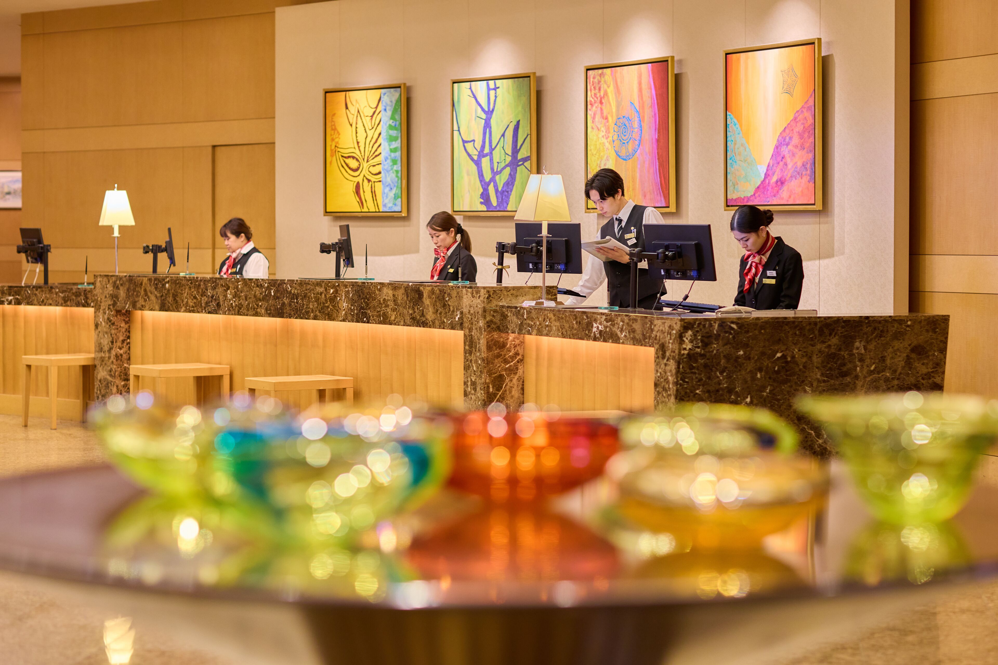A hotel reception area with a marble counter, wooden seating, and colorful artwork on the walls.