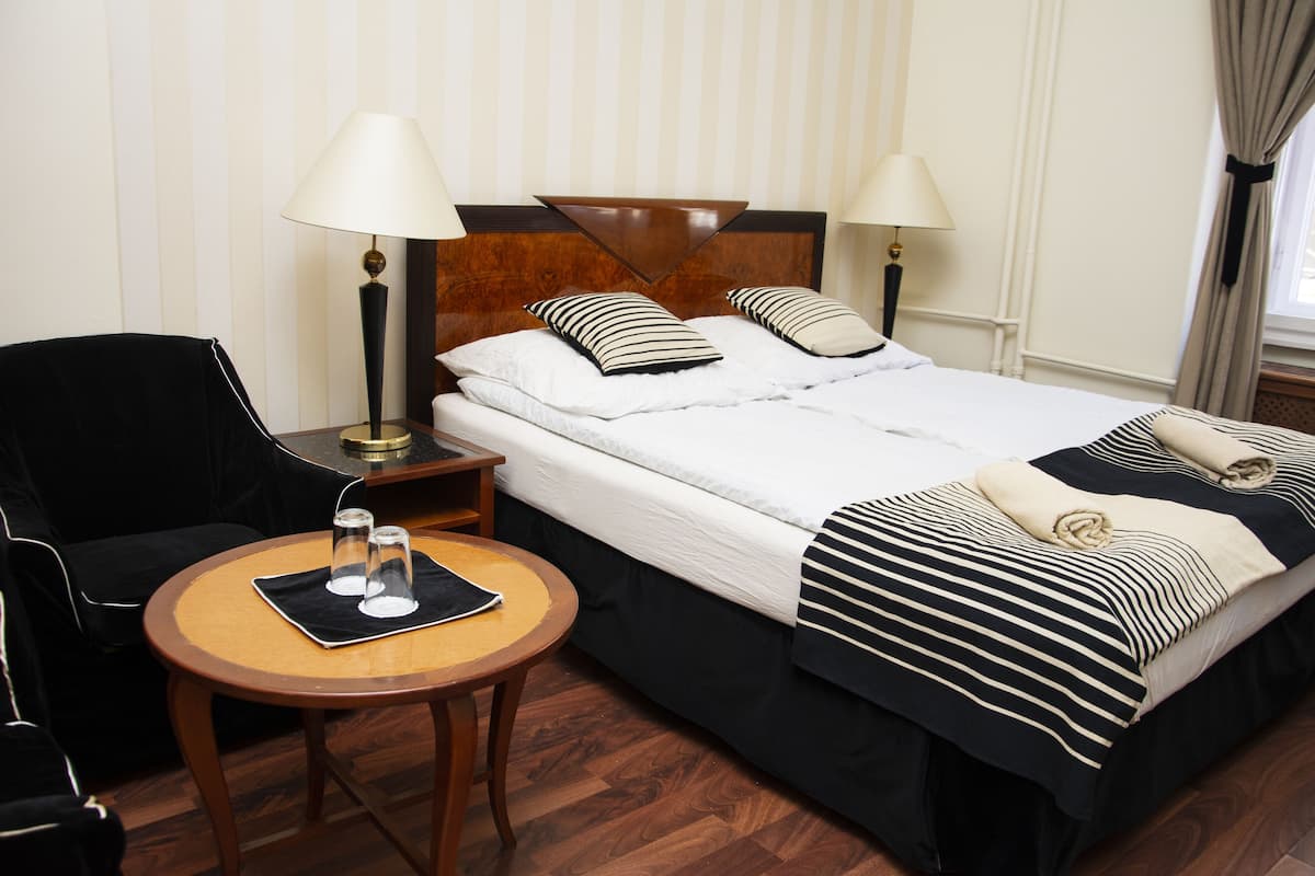 Une chambre d’hôtel avec un lit double, deux tables de chevet, une chaise et une petite table ronde avec deux verres.