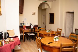 Een eethoek met een ronde houten tafel en stoelen, een rode tafelkleed en een kleine bloemstelling.