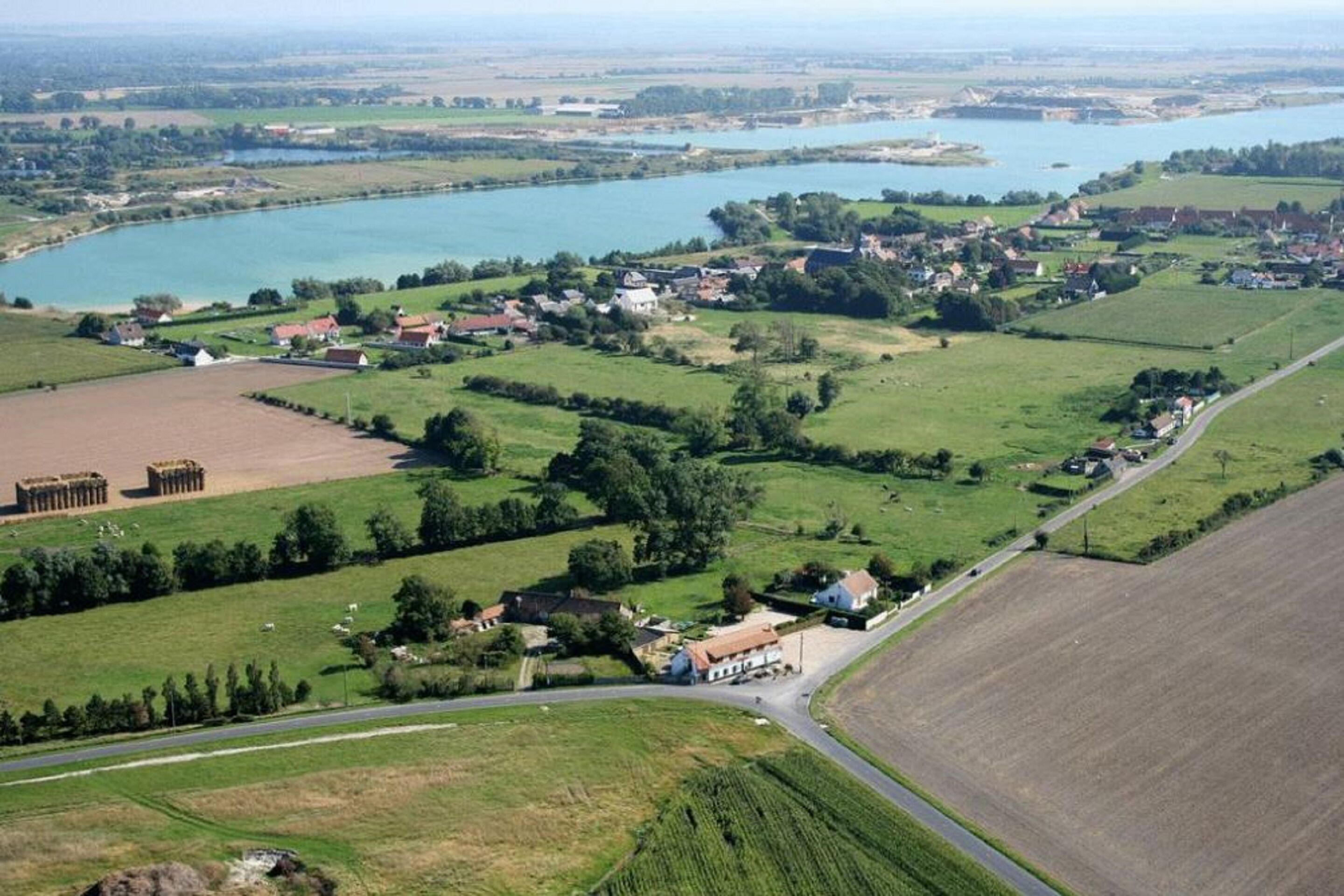 Un paisaje rural con un pequeño pueblo, campos y un lago.