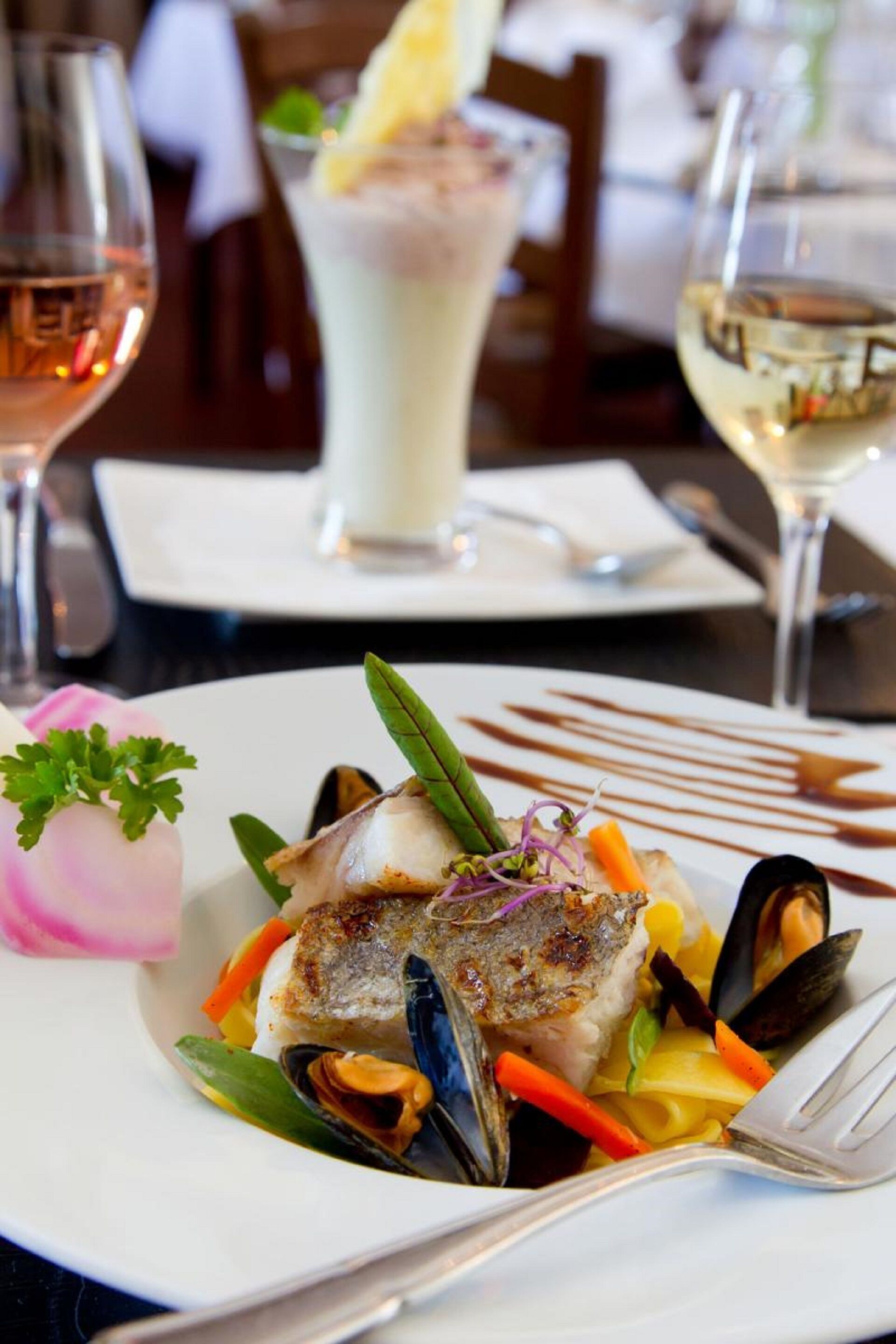 A dining table with a plate of seafood, a glass of white wine, and a dessert drink.
