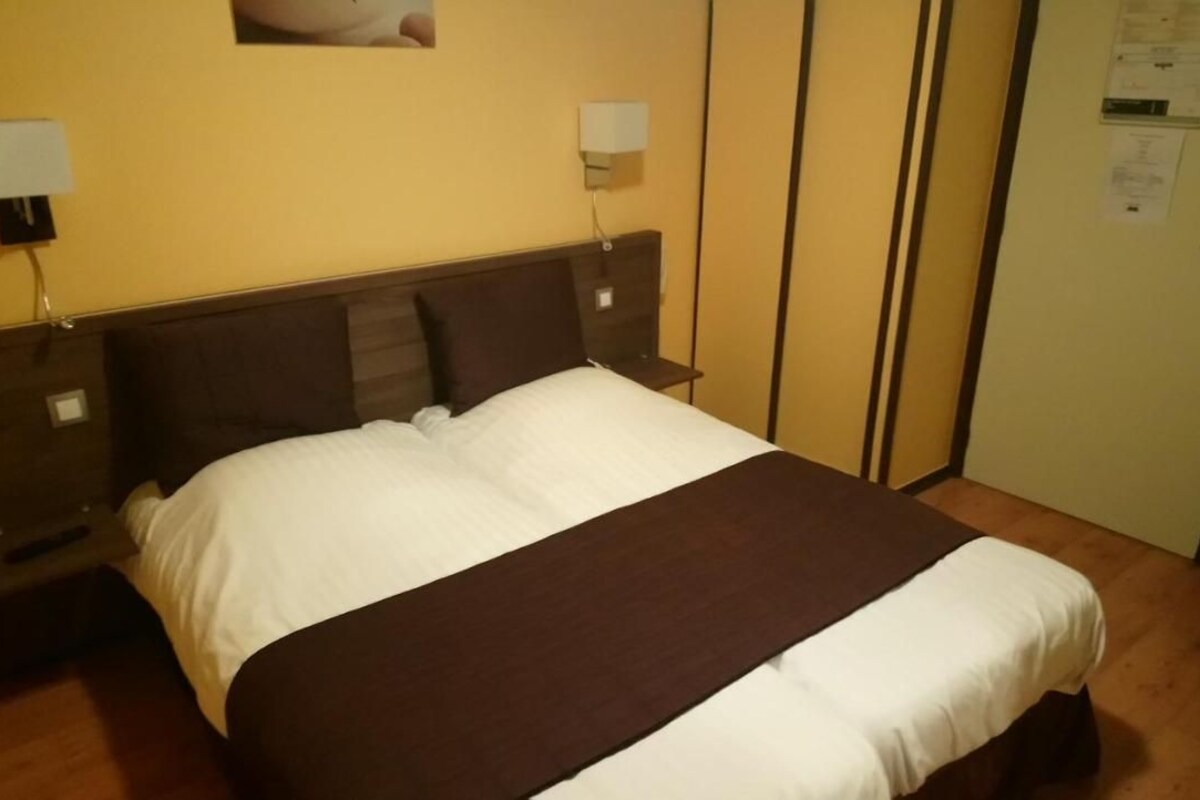 Una habitación de hotel con cama, mesitas de noche, armario y espejo.