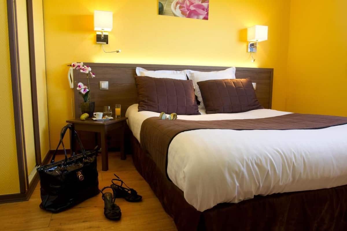Una habitación de hotel con una cama, mesitas de noche, una lámpara, un bolso de mano y un par de zapatos.