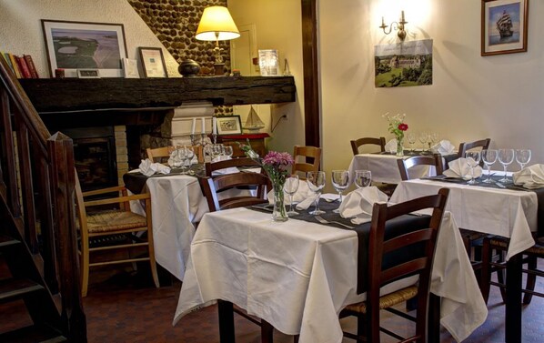 Comedor con mesas dispuestas para una comida, chimenea y cuadros en las paredes.