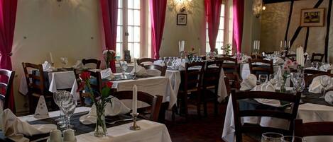 Un restaurante con varias mesas dispuestas para comer, con manteles blancos, velas y centros de mesa florales.