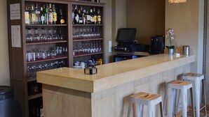 Zona de bar con mostrador de madera, taburetes, estante para vinos y licores, y lámparas colgantes de mimbre.