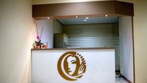 Un mostrador de recepción con un logotipo, una planta en maceta y una escalera al fondo.