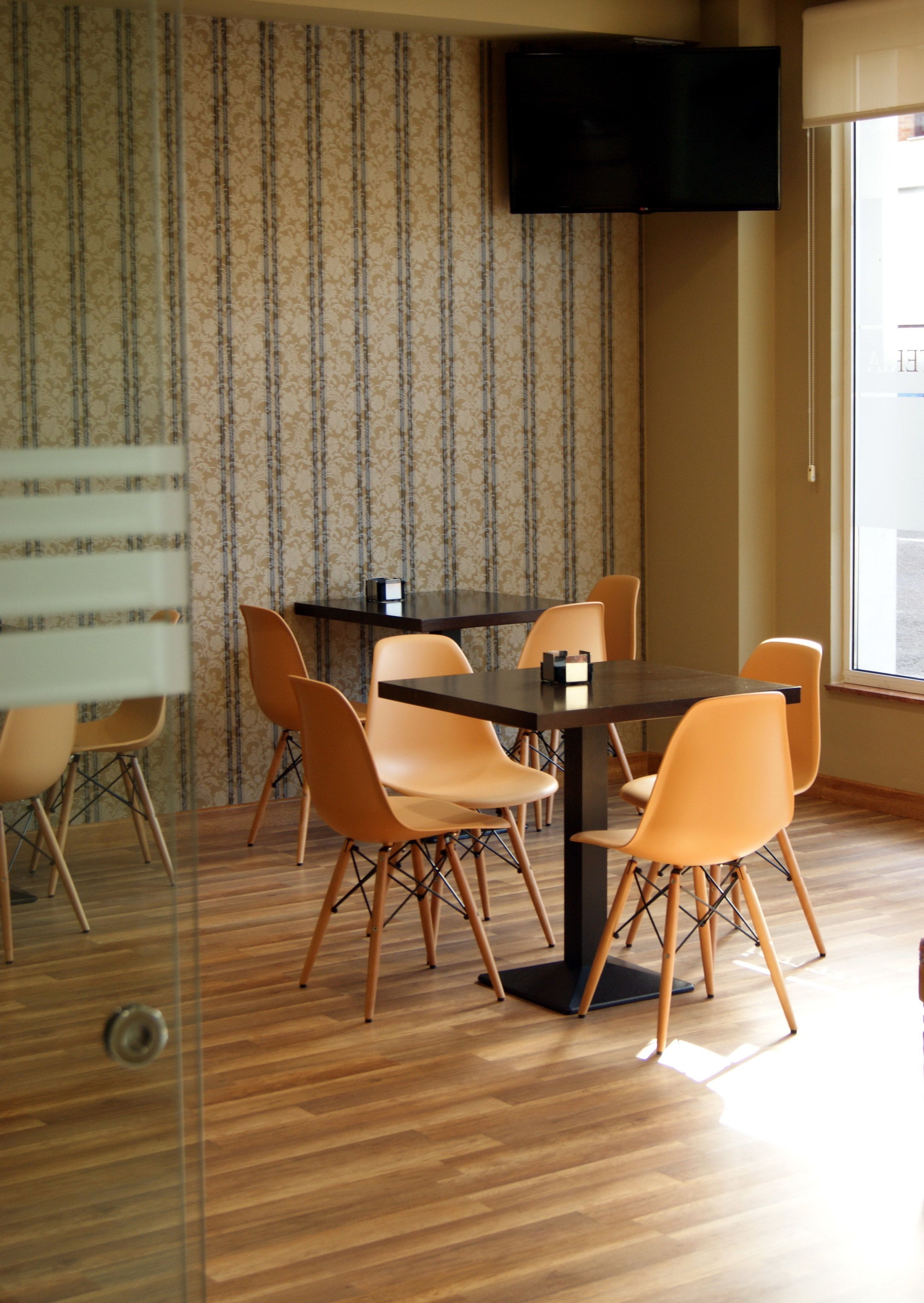 A dining area with a table and chairs, a television mounted on the wall, and a window providing natural light.