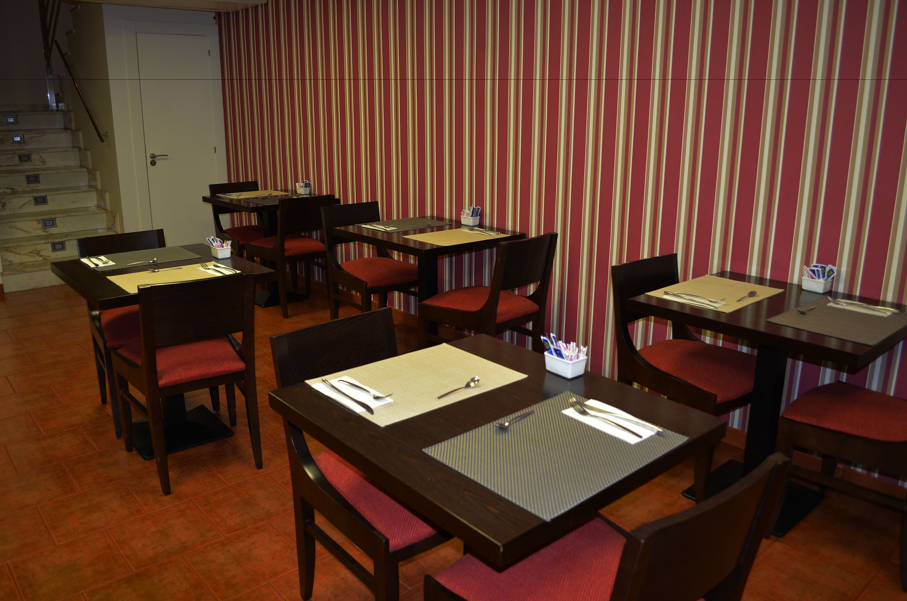 A restaurant with multiple tables and chairs, each set with a placemat, cutlery, and a small container of utensils.