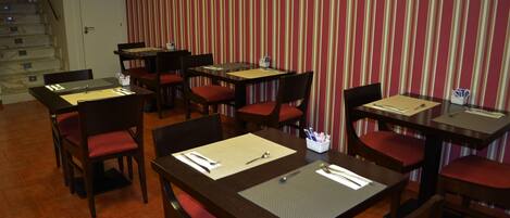 A restaurant with multiple tables and chairs, each set with a placemat, cutlery, and a small container of utensils.
