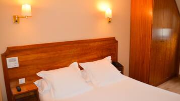 A hotel room with a wooden headboard, two bedside lamps, a bedside telephone, and a wardrobe.