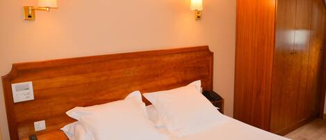A hotel room with a wooden headboard, two bedside lamps, a bedside telephone, and a wardrobe.
