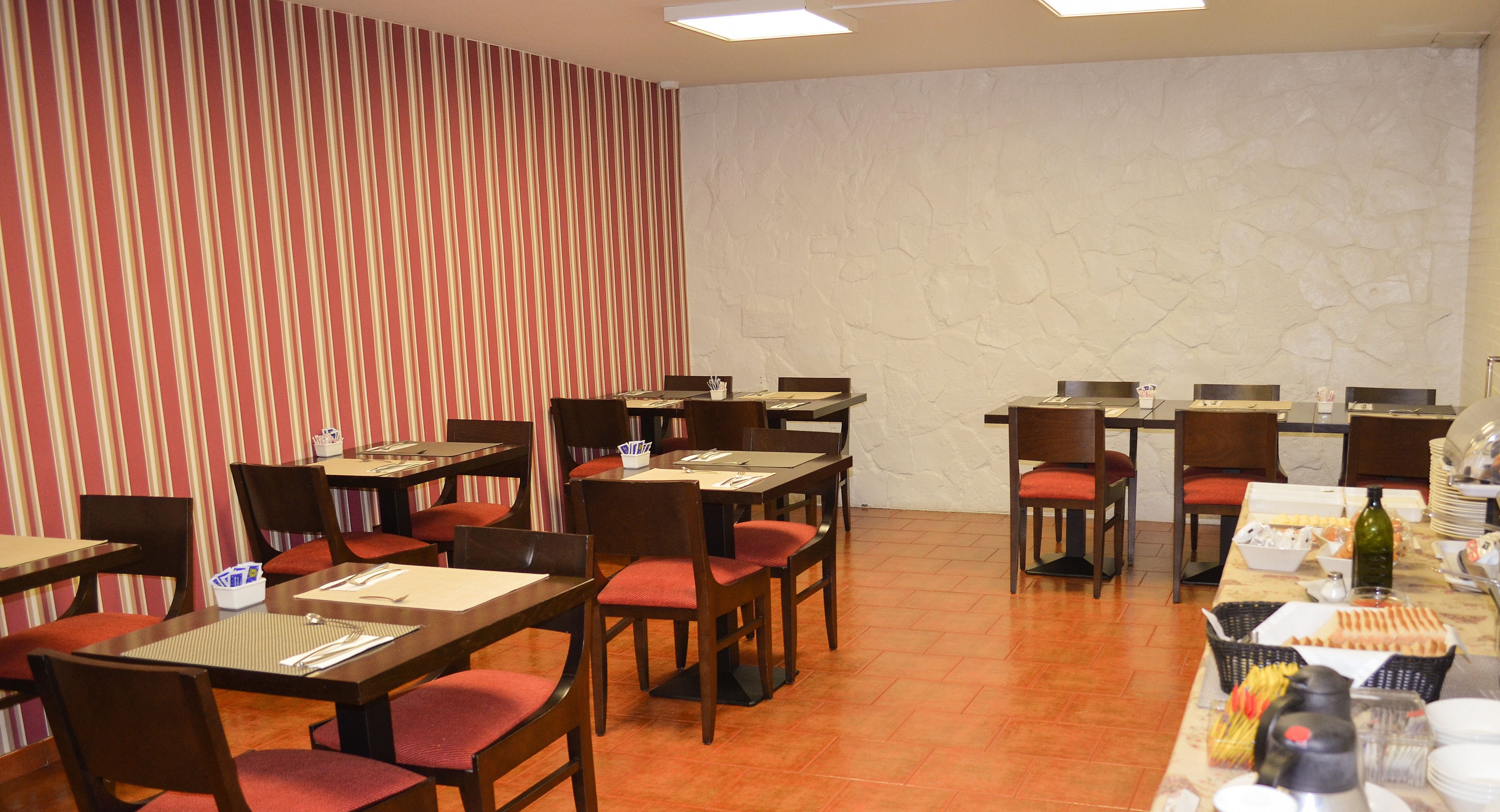 A hotel dining area with striped wallpaper, stone-textured walls, and multiple tables with chairs.