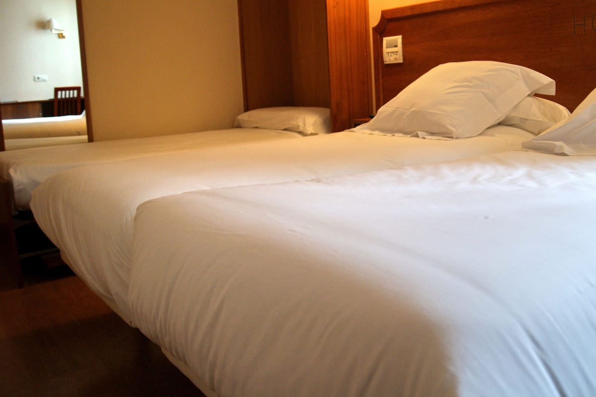 Quarto de hotel com duas camas de solteiro, cabeceira de madeira e uma pequena mesa de cabeceira.