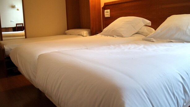 Una habitación de hotel con dos camas individuales, cabecera de madera y una mesita de noche.