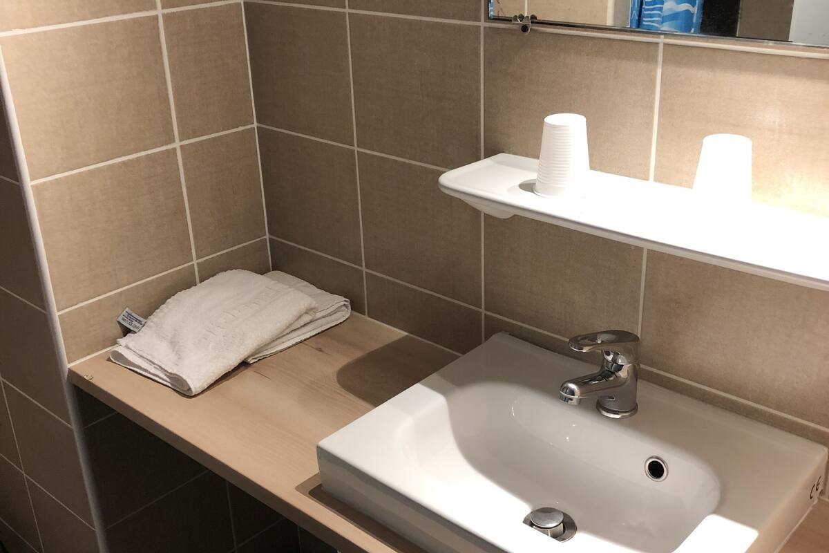 Un baño con un lavamanos blanco, una toalla en el mostrador y un espejo sobre el lavamanos.