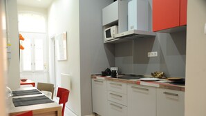 Eine moderne Küche mit grauen Schränken, einer Mikrowelle und einer Kaffeemaschine. Ein Esstisch mit roten Stühlen und ein Fenster mit Vorhängen sind ebenfalls vorhanden.