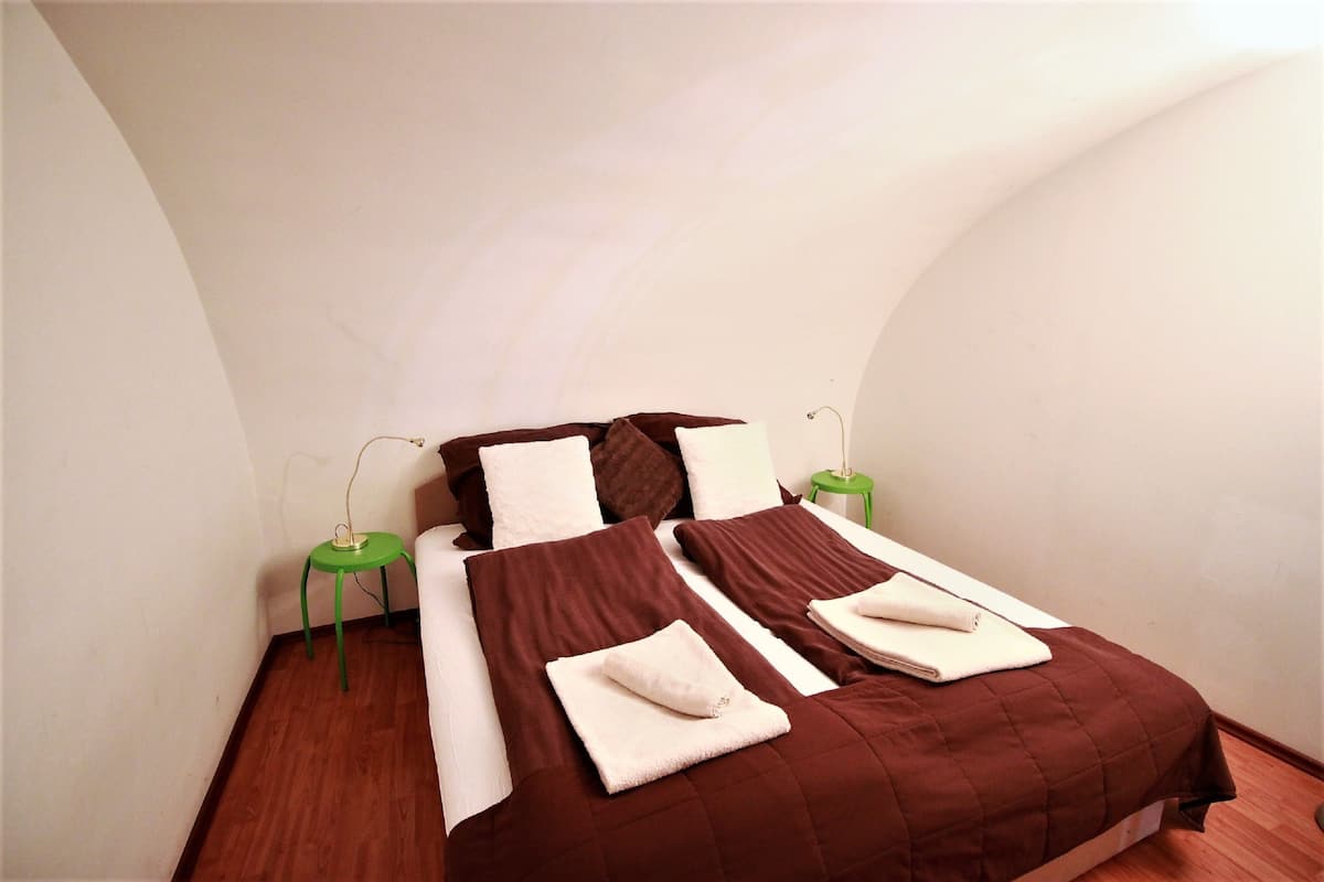 A single bed with brown bedding, white pillows, and a green side table.