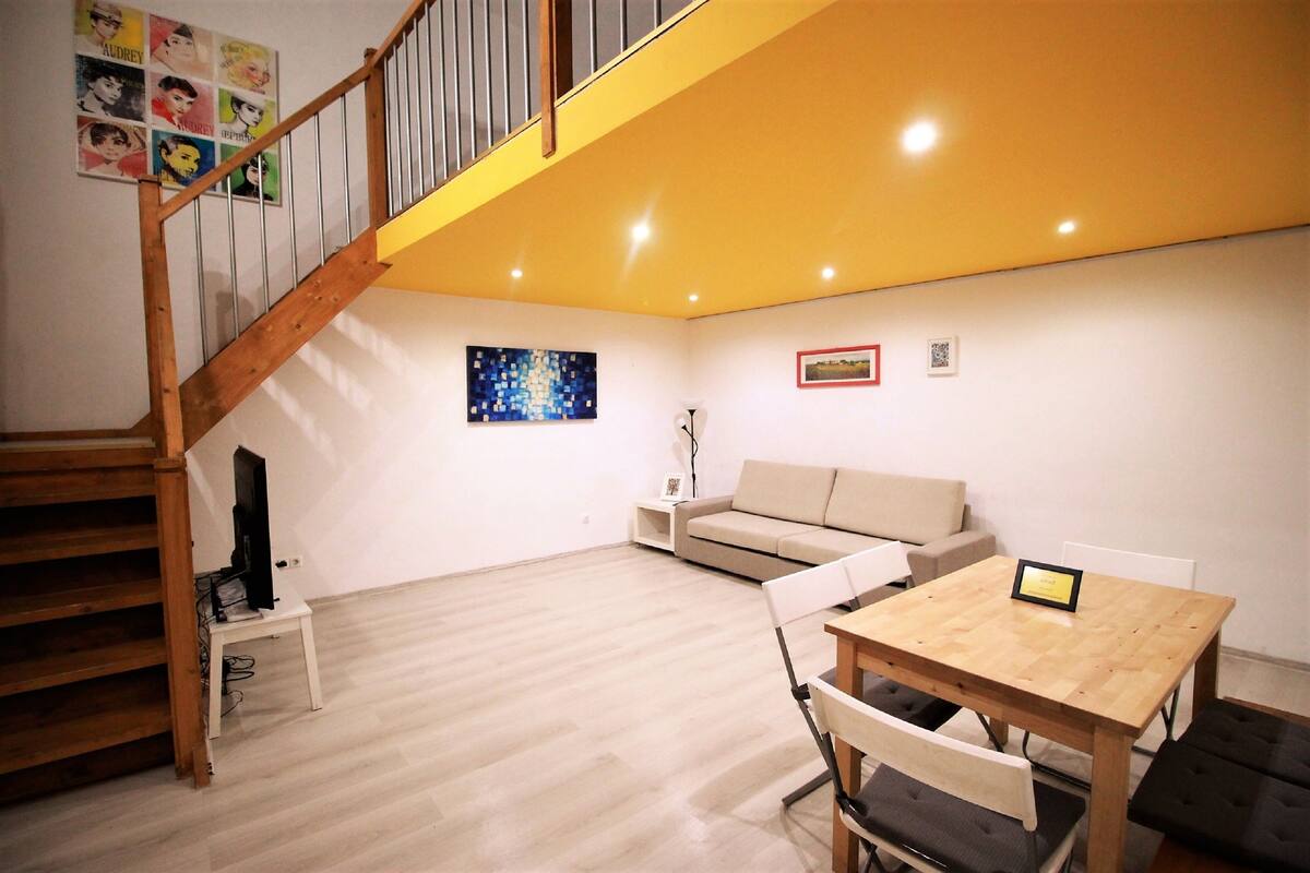 A living room with a wooden staircase, a sofa, a small table, and a television on a stand.