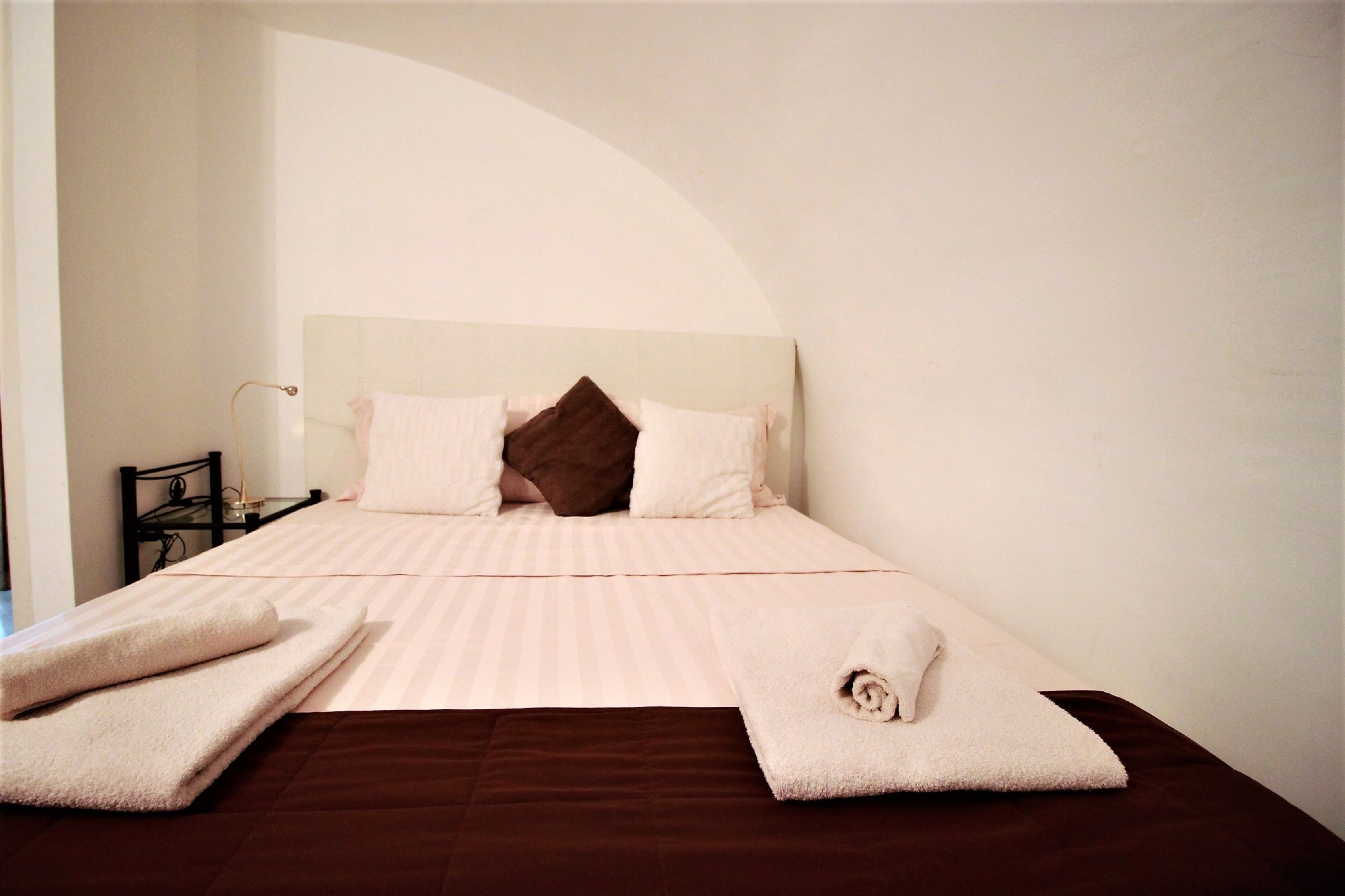 A neatly made bed with a striped bedspread, pillows, and rolled towels.