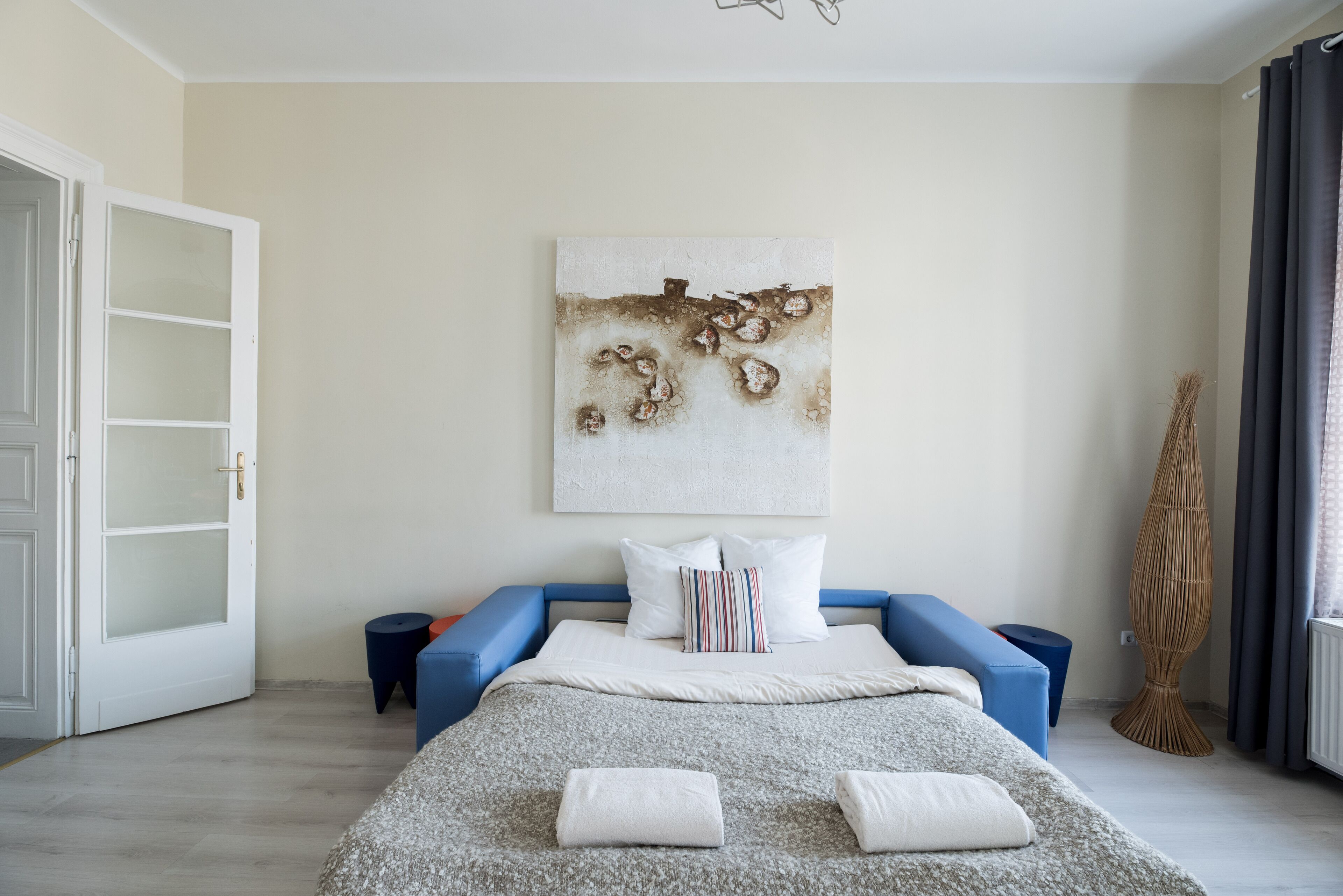 Un dormitorio moderno con una cama, un sofá azul, un cuadro abstracto grande y un jarrón alto.