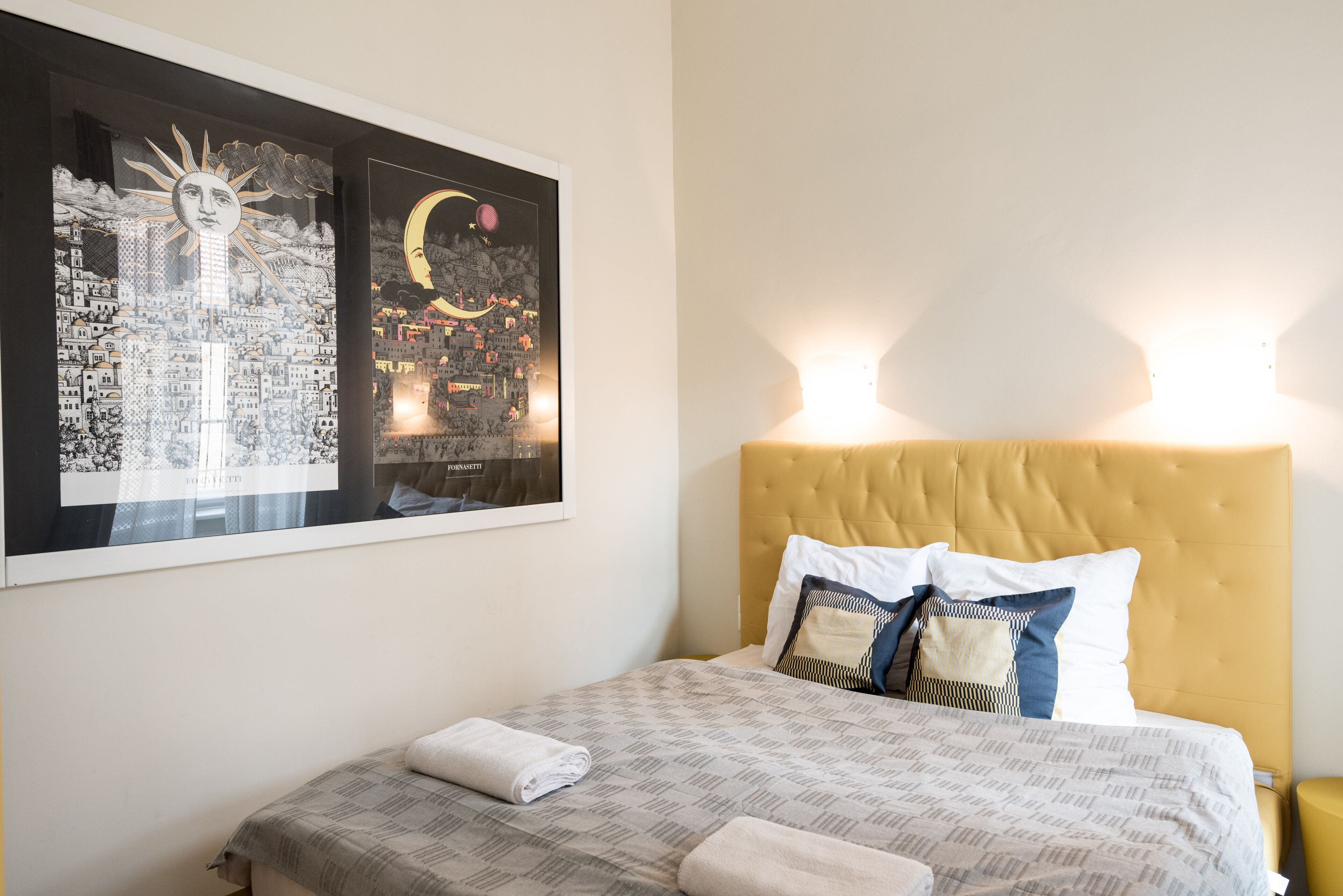 Een netjes opgemaakt bed met een bedsprei en kussens met een patroon, een hoofdbord en twee wandlampen.