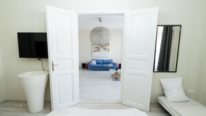 Una habitación con una cama, un sofá blanco, un televisor y un espejo grande.