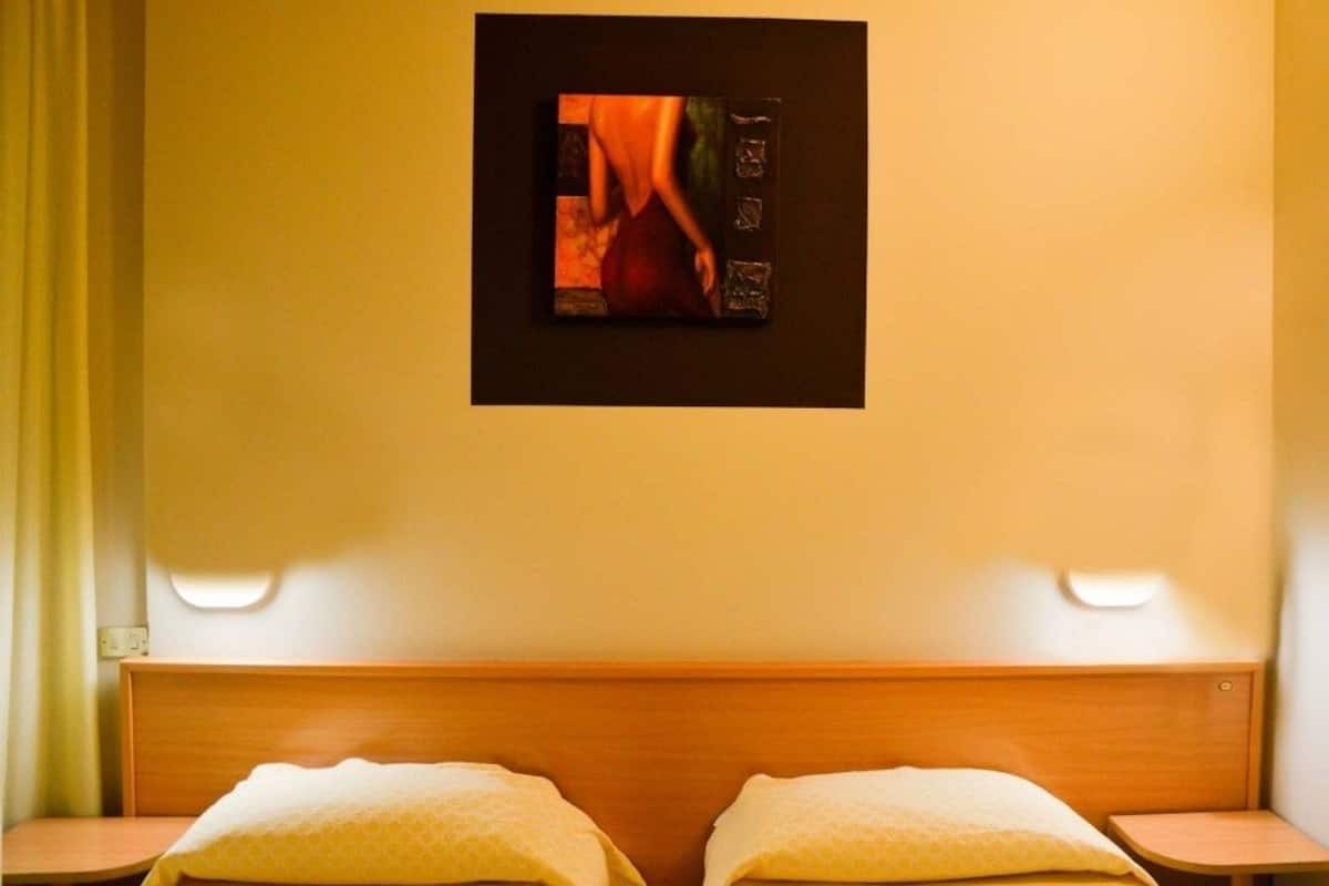 A hotel room with a wooden headboard, two bedside tables, and a wall-mounted painting.