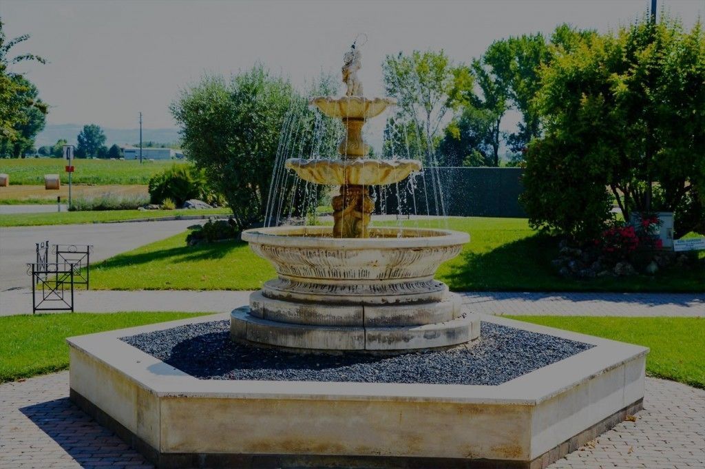 Ein mehrstufiger Brunnen mit Wasserspeiern, umgeben von einer quadratischen Steinsäule und Kies.