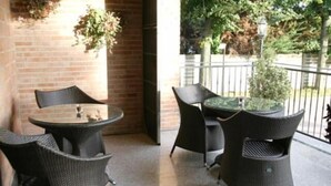 An outdoor patio area with wicker furniture, including a round table and chairs, and a potted plant. - Albergo Aurora (Castenaso)