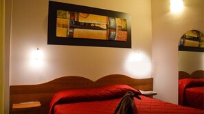 A hotel room with a wooden headboard, a red bedspread, a painting above the bed, and two wall-mounted lights. - Albergo Aurora (Castenaso)