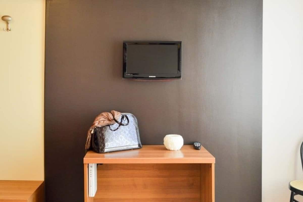A room with a wooden table, a television mounted on the wall, a handbag, and a small white object on the table.